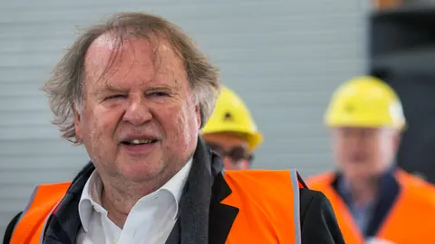 Ein älterer Herr mit orangefarbener Weste.