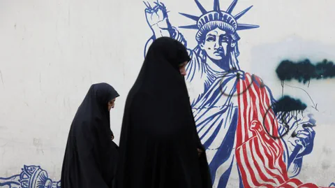 Zwei Personen in schwarzer Kleidung vor einer Freiheitsstatuen-Wandmalerei.
