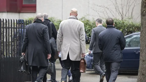 Mehrere Menschen in Mänteln gehen auf einem Bürgersteig.