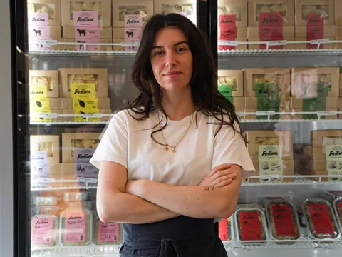 Person mit verschränkten Armen vor einem Kühlregal mit Produkten.