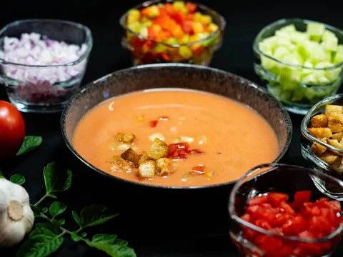 Schüssel mit Suppe, umgeben von Gemüse und Croûtons in kleinen Schalen.