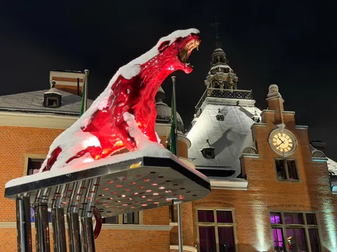 Eine rote Statue, ein Panther mit weit geöffneter Schnauze, vor einem historischen Gebäude bei Nacht.