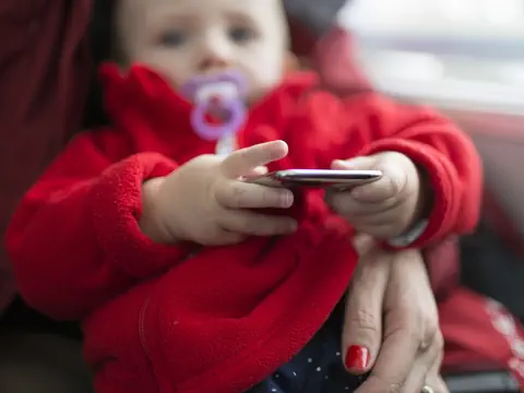 Säugling mit Schnuller hält ein Smartphone.