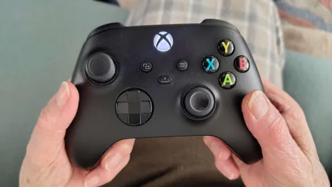 Hände einer älteren Dame halten einen schwarzen Gamecontroller