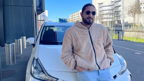 Mann mit Sonnenbrille lehnt an weissem Taxi.