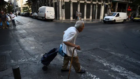 Ein älterer Mann mit seinem Einkaufscaddy überquert eine Strasse in Athen.