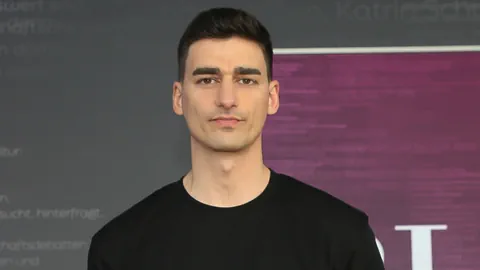 Person mit dunklen Haaren vor einem dunkelgrauen und lila Hintergrund.