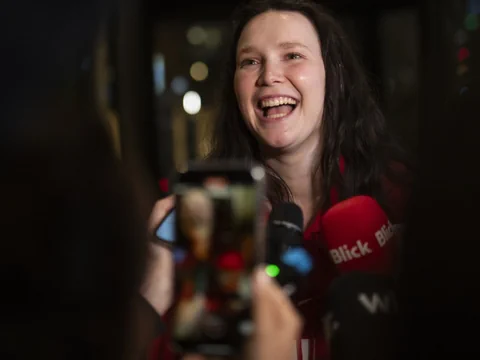 Eine junge Frau lacht und ist umringt von Mikrofonen