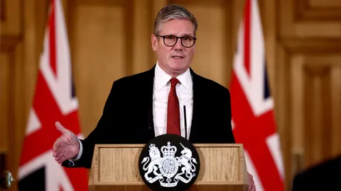 Keir Starmer spricht hinter einem Pult mit zwei britischen Flaggen im Hintergrund.