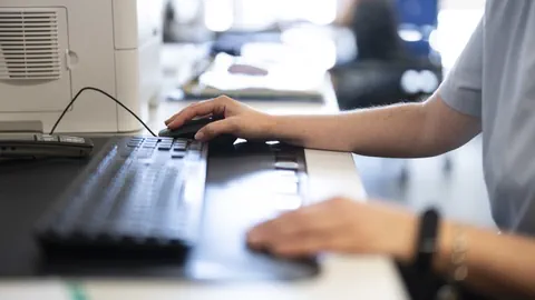 Person tippt auf Tastatur an einem Schreibtisch.