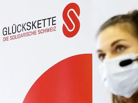 Frau mit Kopfhörern vor dem Emblem der Schweizer Glückskette.