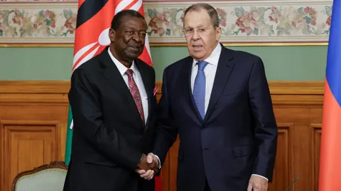 Russlands Aussenminister Sergei Lawrow (rechts) und Kenias Aussenminister Musalia Mudavadi (links) geben sich nach Gesprächen in Moskau die Hand.Hinter ihnen sind die Flaggen Russlands und Kenias zu sehen. Die Szene wirkt formell, es handelt sich um eine gemeinsame Pressekonferenz nach politischen Gesprächen. 