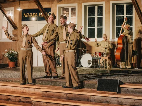 Sechs Personen in Uniformen treten auf einer Bühne mit Musikinstrumenten auf.