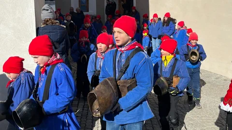 Kinder in blauen Hemden mit roten Zipfelmützen und Glocken.