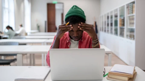 Person sitzt nachdenklich vor Laptop in Bibliothek.