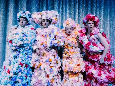 Vier Personen in Blumenkleidern auf einer Bühne.