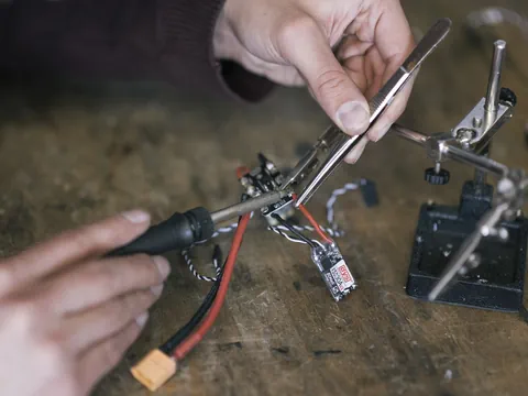 Ein Mensch hält ein Reagenzglas in der Hand, trägt blaue Silikonhandschuhe und im Hintergrund sind Maschinen zu sehen.