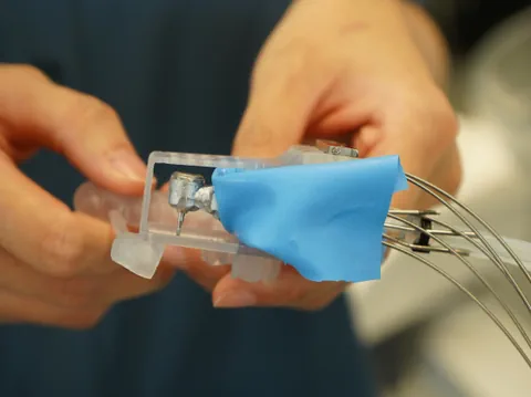 Nahaufnahme von Händen, die ein kleines technisches Gerät mit blauer Abdeckung halten.