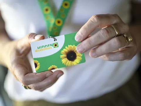 Person hält eine Karte mit Sonnenblume und Text 'Hidden Disabilities'.