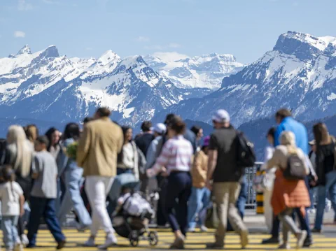 Menschen überqueren Strasse mit schneebedeckten Bergen im Hintergrund.