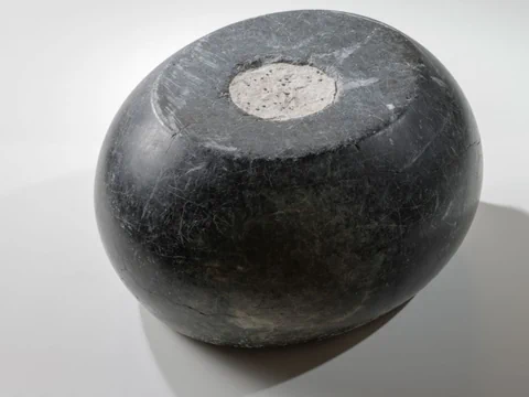 Rundes schwarzes Steingefäss mit flacher Oberseite.