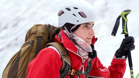 Laila Grillo unterwegs in Klettermontur mit weissem Helm und roter Jacke.