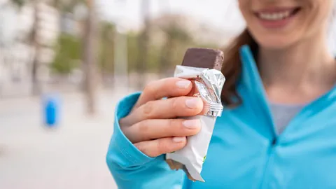 Frau in Sportkleidung hält Proteinriegel.