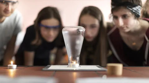 Kinder beobachten wissenschaftliches Experiment mit Kerzen und Glas.