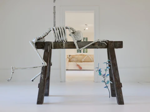 Skelettskulptur auf Holztisch vor Türöffnung.