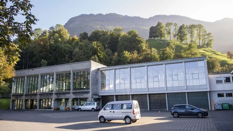 Moderne Gebäude vor bewaldetem Hügel.
