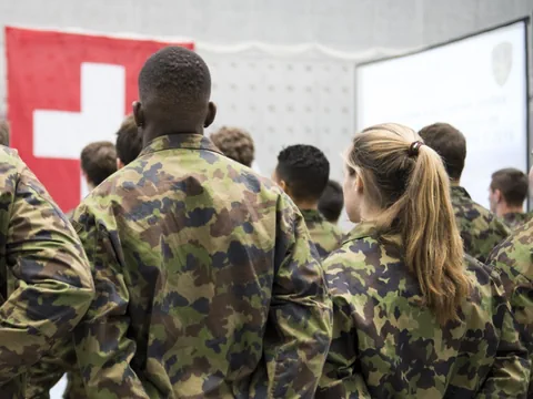Junge Personen stehen im Militäranzug vor einer Schweizer Flagge.