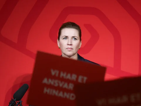 Eine Frau mit ernsthaftem Gesichsausdruck vor einem roten Hintergrund.