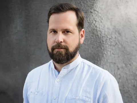 Mann mit Bart vor grauem Hintergrund.