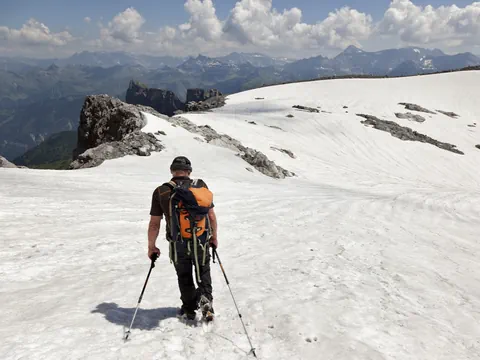 Wanderer mit Rucksack auf schneebedecktem Berghang.