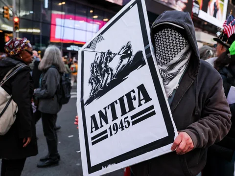 Person mit Kopftuch hält ein Schild in einer Menschenmenge bei einer Demonstration.