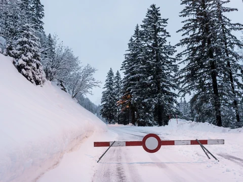 Verschneite Strasse mit Schranke und Tannenbäumen.