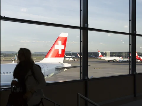 Blick aus dem Flughafengebäude auf parkende Flugzeuge mit Schweizer Flagge.