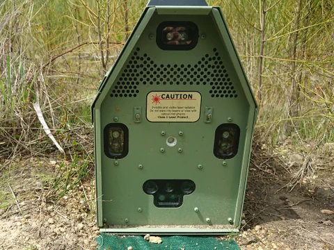 Nahaufnahme eines grünen laserbasierten Geräts im Freien mit Warnschild.