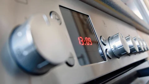 Nahaufnahme von Edelstahl-Ofenknöpfen und digitaler Uhranzeige.