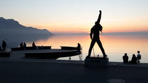 Im Vordergrund ist eine Statue zu sehen. Im Hintergrund erstreckt sich der Genfer See.