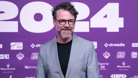 Mann mit Brille vor lila Hintergrund mit 2024-Text.