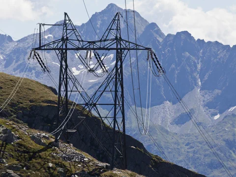 Strommast in bergiger Landschaft mit Gipfeln im Hintergrund.