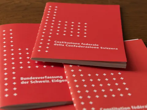 Rote Bücher mit weissen Kreuzen auf einem Tisch gestapelt.