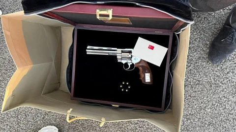 Eine Schachtel mit einem Revolver und einer Karte auf einem schwarzen Hintergrund in einer Papiertüte.