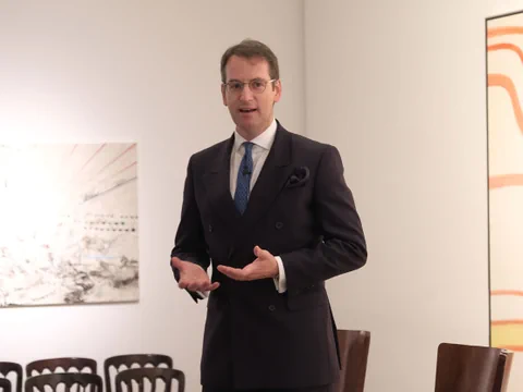 Mann in Anzug spricht in einem Raum mit Stühlen.