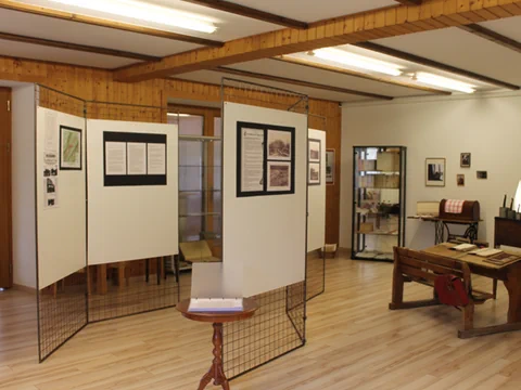 Ein Ausstellungsraum mit Informationstafeln, Holztisch und Stühlen.