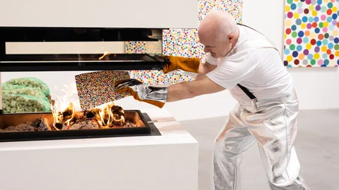 Damian Hirst legt ein Kunstwerk mit bunten Punkten in den Ofen zum Verbrennen.