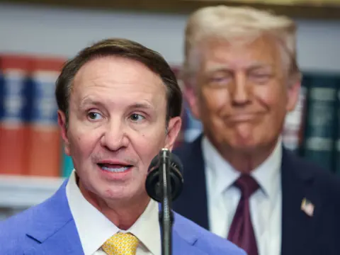 Mann spricht in Mikrofon, andere Person im Hintergrund.