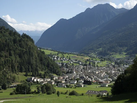 Blick auf ein Dorf in einem alpinen Tal zwischen bewaldeten Bergen.