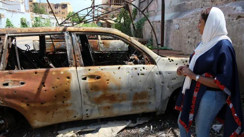 Zerschossenes Auto, eine Frau.